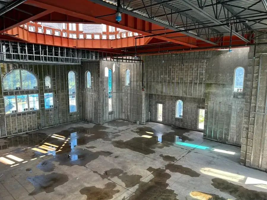 Interior with the orange steel of the dome ring overhead, block walls lined with steel studs, arched window openings and a wet concrete floor