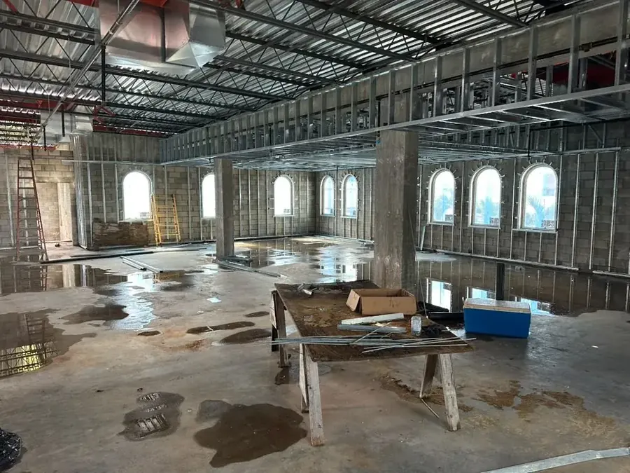 An open floor under steel ceiling joists, a row of arched windows along the block wall, a ladder, a trestle table and stacked materials