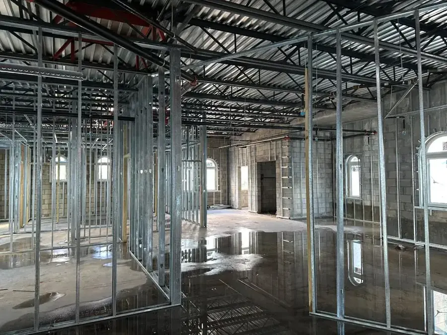 Steel stud framing dividing the side rooms, with ceiling joists overhead and arched windows in the block walls beyond