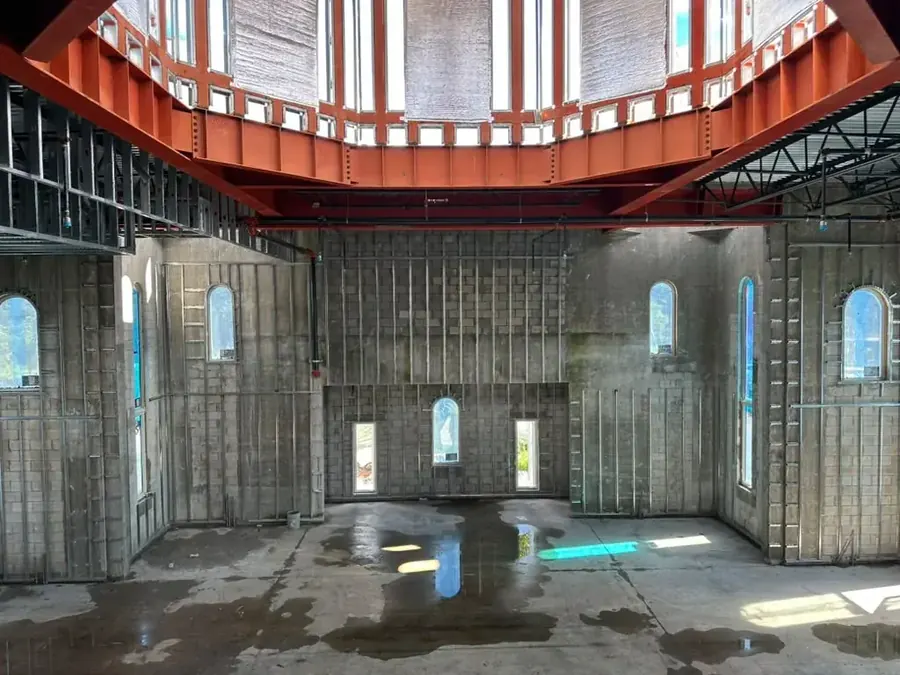 Close view of the dome steelwork: the orange ring and the window frames of the drum directly overhead, above the block walls of the hall